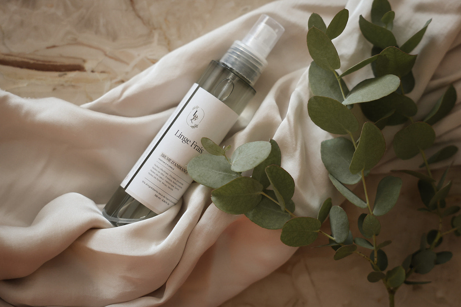 Brume d'ambiance parfumée artisanale et végétale LBL Linge frais sur une table en marbre et drap blanc satiné et feuilles d'eucalyptus.