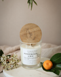 Bougie artisanale parfumée Fleur d'oranger & Musc Les Bougies de Léa avec couvercle en bois d'acacia, sur un support en marbre blanc, avec un drap en lin en arrière plan, accompagnée d'une orange et des fleurs blanches.