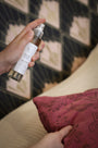 Spray d'ambiance parfumé Fleur de Cerisier LBL pulvérisé sur un coussin en velours rose avec des motifs fleuris.