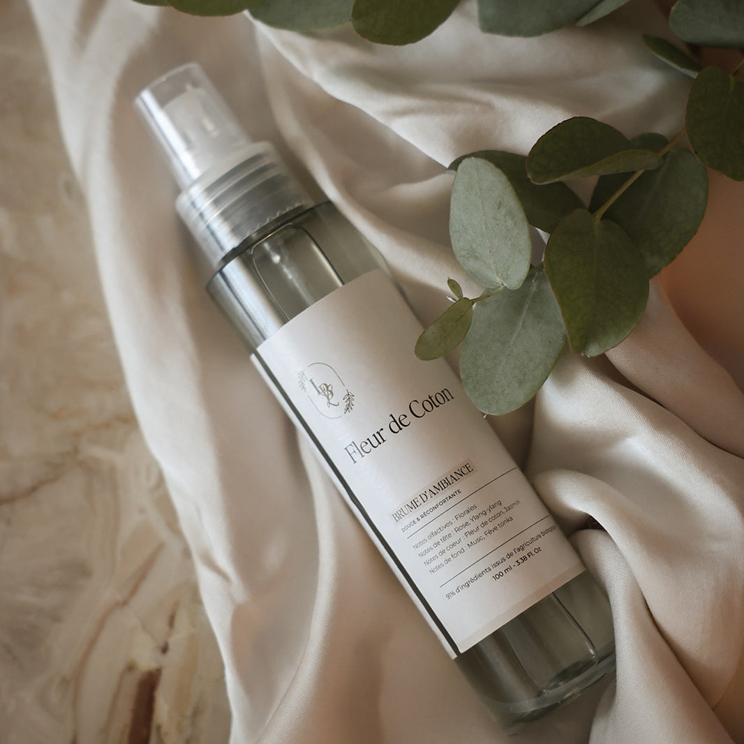 Testeur de brume d'ambiance LBL 30ml parfum Fleur de Coton posé sur un drapé en tissu beige avec des feuilles d'eucalyptus.