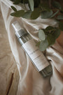 Testeur de brume d'ambiance LBL 30ml parfum Fleur de Coton posé sur un drapé en tissu beige avec des feuilles d'eucalyptus.