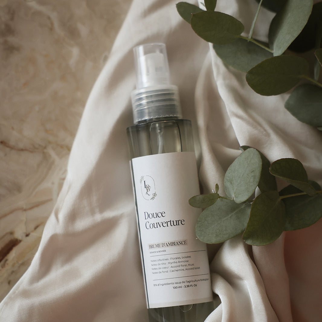 Brume d'ambiance parfumée Douce couverture LBL sur un drapé blanc satinéet feuille d'eucalyptus.