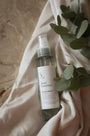 Brume d'ambiance parfumée Douce couverture LBL sur un drapé blanc satinéet feuille d'eucalyptus.