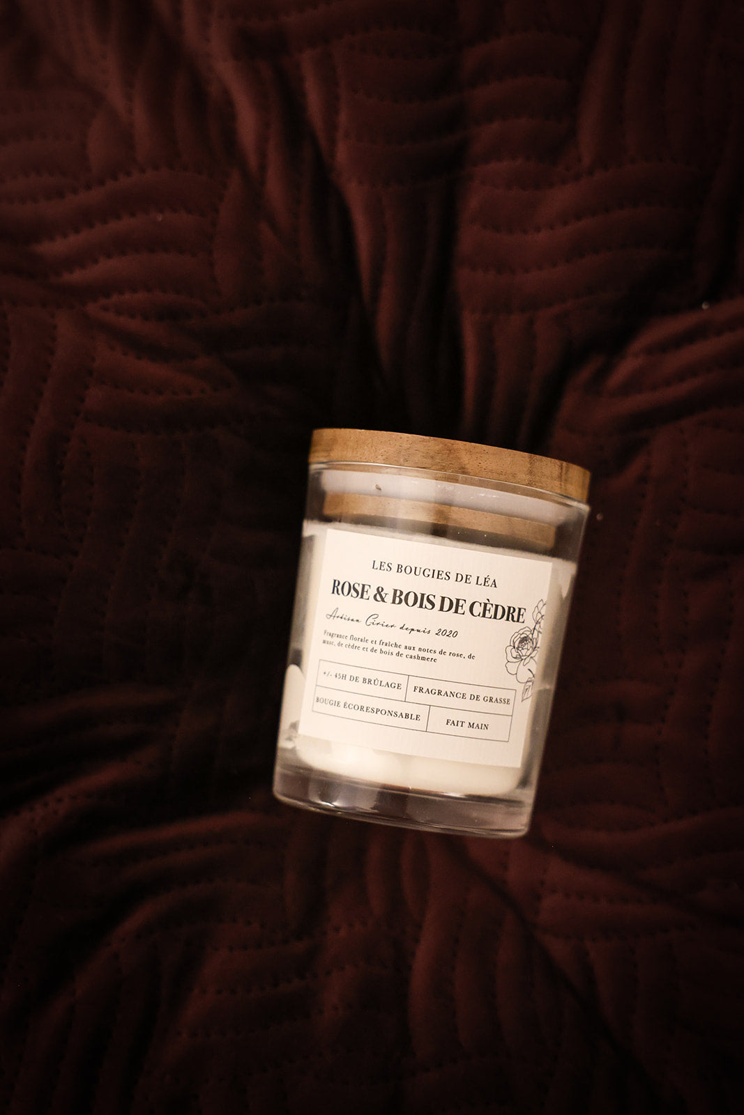 Bougie artisanale parfumée Rose & Bois de Cèdre Les Bougies de Léa sur un coussin en velours bordeau.