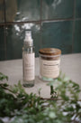 Bougie parfumée Les Bougies de Léa et brume d'ambiance LBL de la senteur Rose & Bois de Cèdre sur un carrelage en marbre, dans une salle de bain, avec feuilles d'olivier.