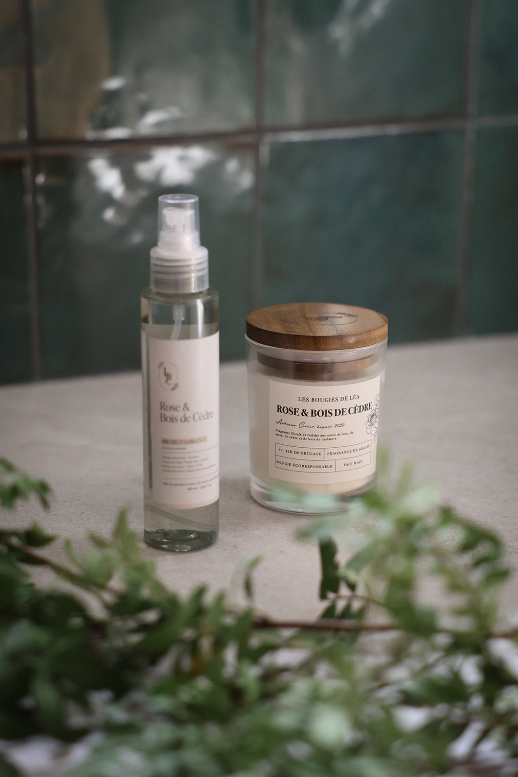 Bougie parfumée Les Bougies de Léa et brume d'ambiance LBL de la senteur Rose & Bois de Cèdre sur un carrelage en marbre, dans une salle de bain, avec feuilles d'olivier.