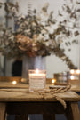Bougie parfumée artisanale Les Bougies de Léa Fleur de Cerisier allumée, posée sur un tabouret en bois et branche de blé séché et feuilles d'eucalyptus en fond.