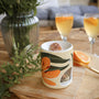 Brûle-parfum en céramique aux motifs floraux, fleur de Lys et estival, avec un fondant parfumé artisanal LBL et une bougie chauffe-plat, en extérieur avec oranges et cocktails.