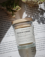 Bougie artisanale parfumée Fleur de Cerisier Les Bougies de Léa sur un livre ouvert et fleurs blanches, avec rayons de soleil