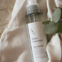 Brume d'ambiance parfumée LBL Douce Couverture sur un drapé blanc satiné avec feuille d'eucalyptus.