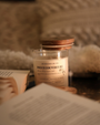 Bougie parfumée Douce couverture Les Bougies de Léa sur une table accompagnée de livre ouverts et coussin blanc en fond.