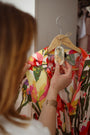Femme qui suspend une suspension végétale parfumée LBL Mandarine, citron vert bergamote à un cintre sur une robe colorée et estivale pour parfumer sa penderie, son dressing ou son placard.