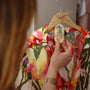 Femme qui suspend une suspension végétale parfumée LBL Mandarine, citron vert bergamote à un cintre sur une robe colorée et estivale pour parfumer sa penderie, son dressing ou son placard.
