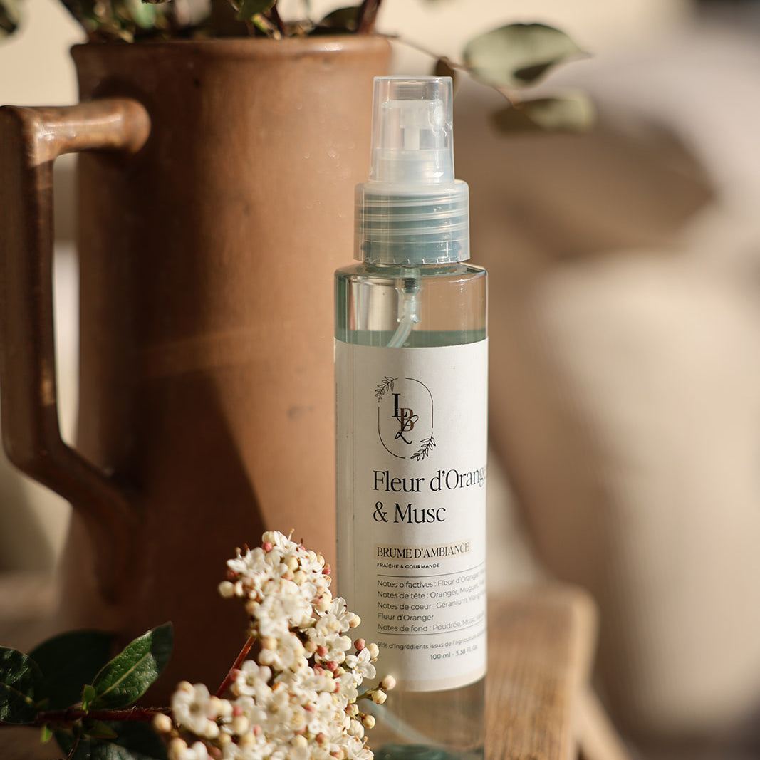 Brume d'ambiance parfumée Fleur d'oranger & Musc LBL sur une table en bois avec fleurs blanches et vase en terre cuite, à la lumière du coucher de soleil.
