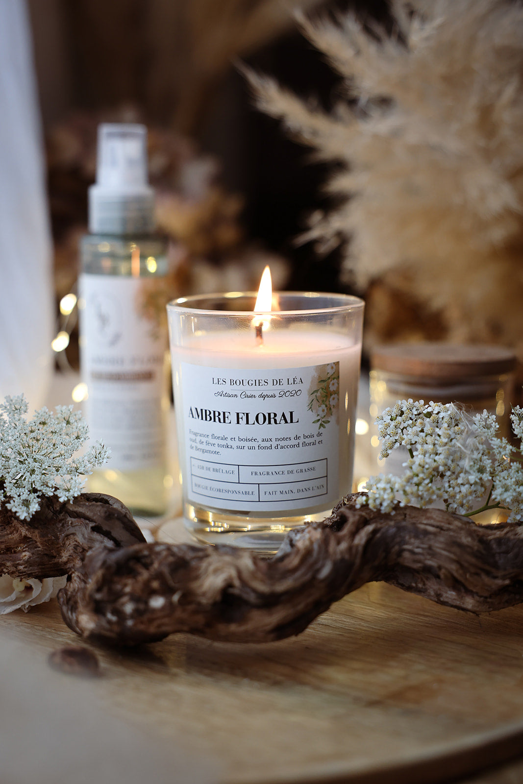 Bougie artisanale parfumée Les Bougies de Léa Ambre Floral Bois de Oud allumée, décor bohème chic, fleurs blanches, branches bois, pampa