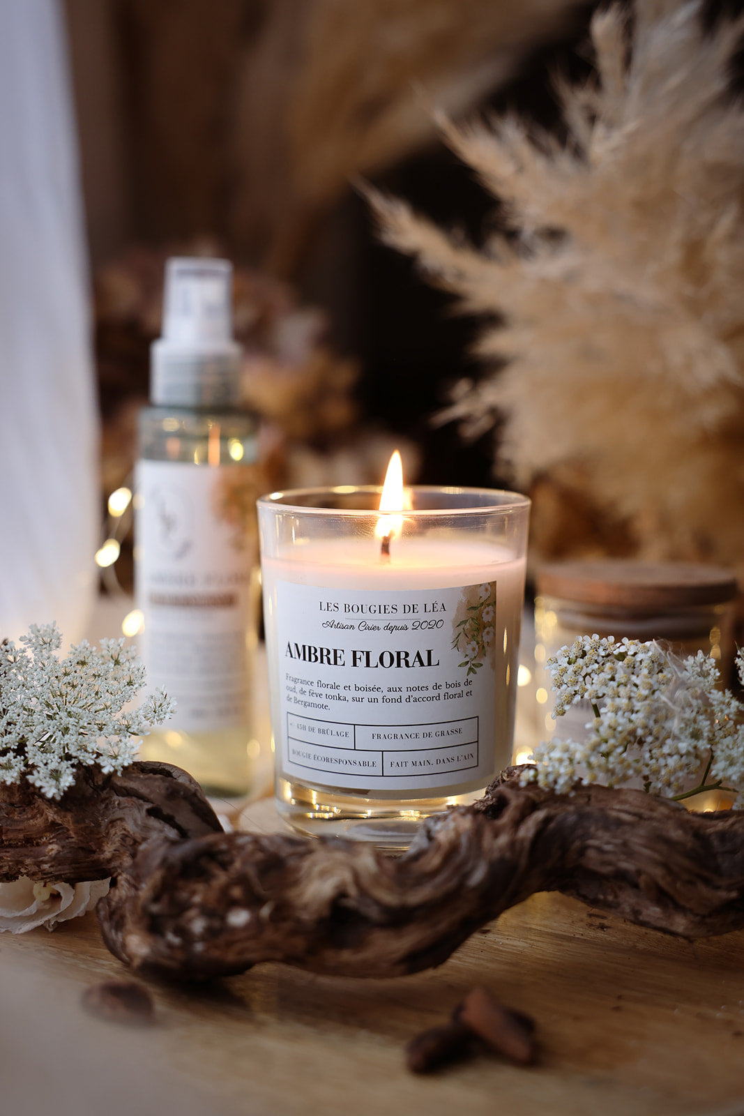 Bougie artisanale parfumée Ambre Floral Les Bougies de Léa allumée avec fleurs blanches et branche de bois, dans un déco bohème chic