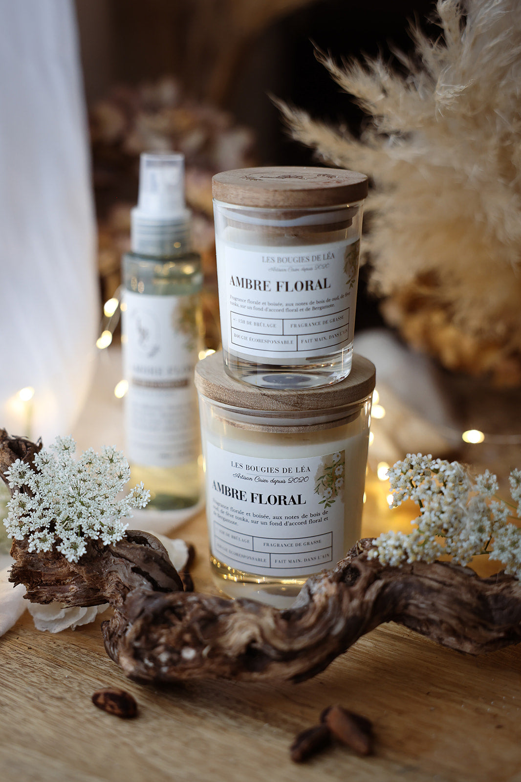 Bougies artisanales parfumées Ambre Floral avec couvercle en bois d'Acacia Les Bougies de Léa empilées avec fleurs blanches et branche de bois, dans un déco bohème chic