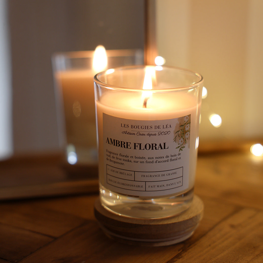 Bougie artisanale parfumée Les Bougies de Léa Ambre Floral Bois de Oud allumée sur meuble en bois devant miroir et guirlande lumineuse