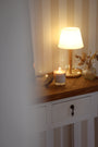 Bougie artisanale parfumée Ambre Floral Les Bougies de Léa allumée sur meuble en bois d'entrée comme objet de décoration d'intérieur et lampe allumée et vase de fleurs séchées