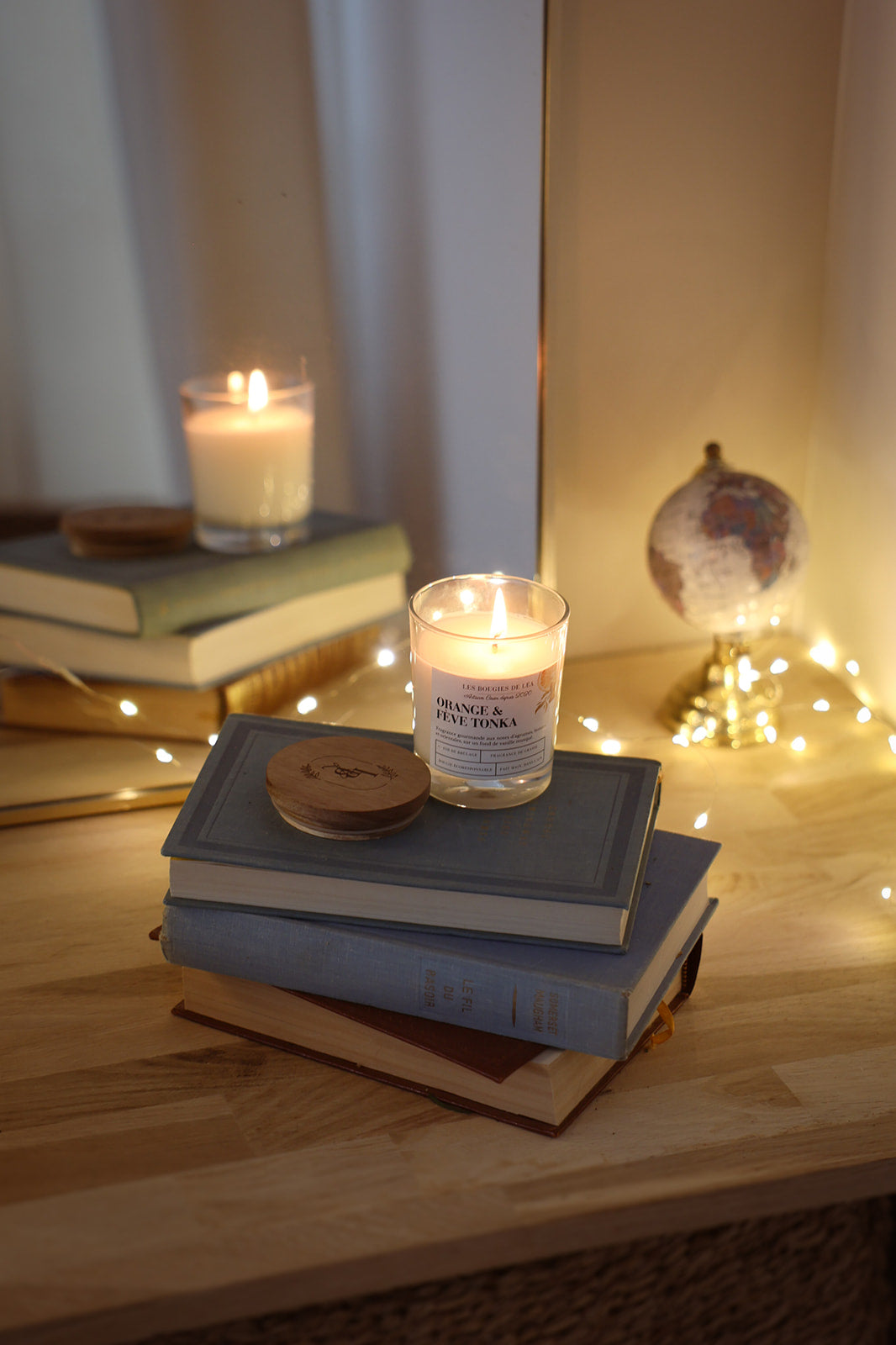 Bougies artisanales parfumées Orange et fève Tonka, orange cannelle allumée avec couvercles en bois d'acacia, sur livres, déco bohème chic, guirlande lumineuse.