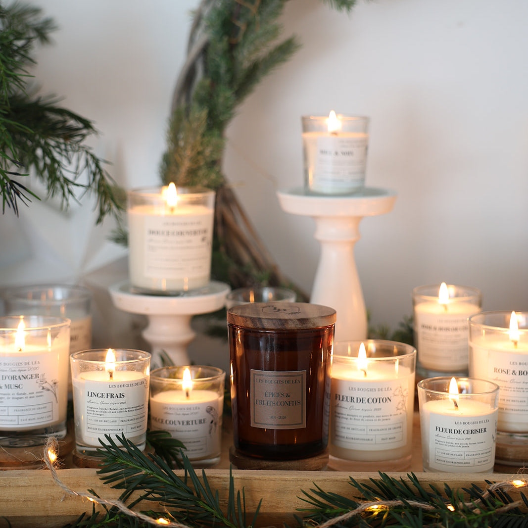 Bougies artisanales parfumées Les Bougies de Léa allumées sur une cheminée, décorées de guirlandes lumineuses et sapin