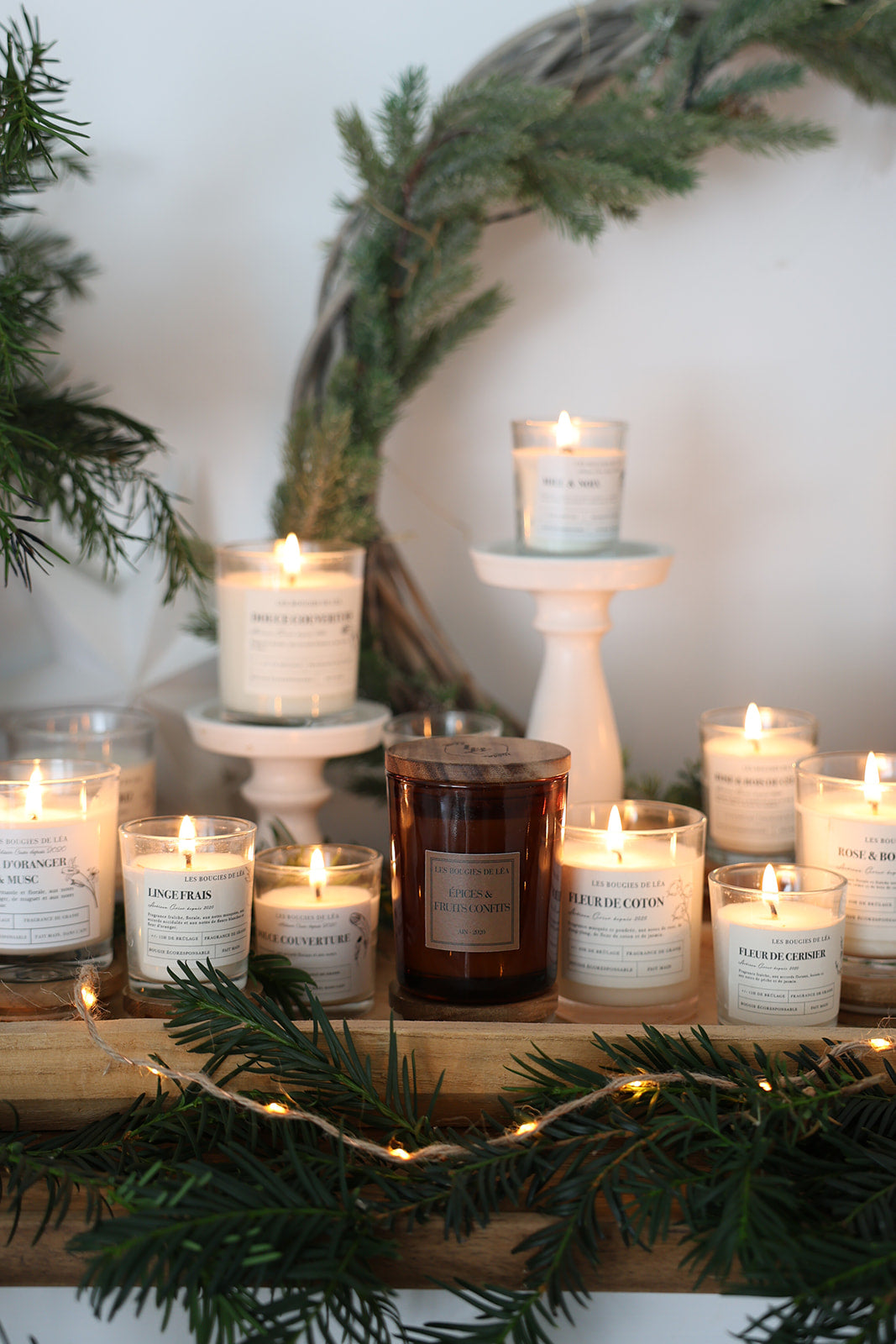 Bougies artisanales parfumées Les Bougies de Léa allumées sur une cheminée, décorées de guirlandes lumineuses et sapin