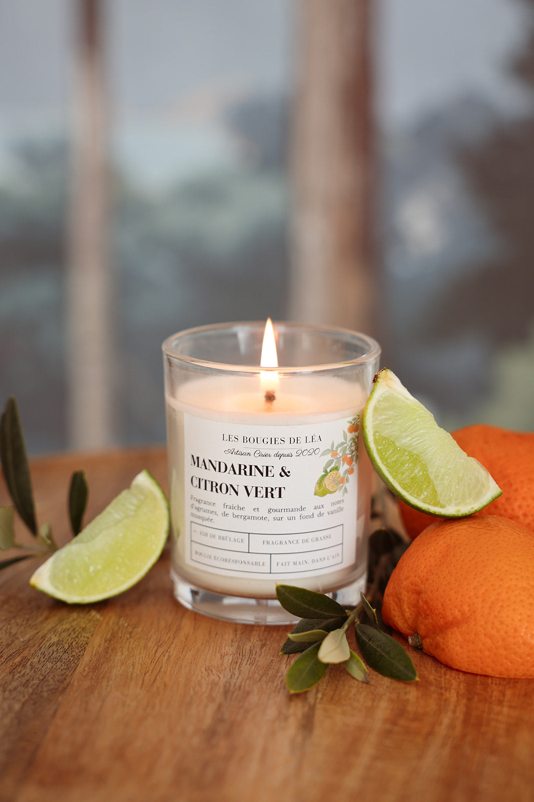 Bougie artisanale parfumée Mandarine & Citron vert Bergamote Les Bougies de Léa allumée, accompagnée d'agrumes, oranges, citron vert et feuilles d'olivier.