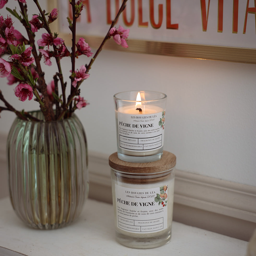 Bougies artisanales parfumées Les Bougies de Léa Pêche de vigne, sur une cheminée bohème chic, accompagnées d'un vase de Fleurs de Cerisier et un table au mur "Dolce Vita" terracotta.