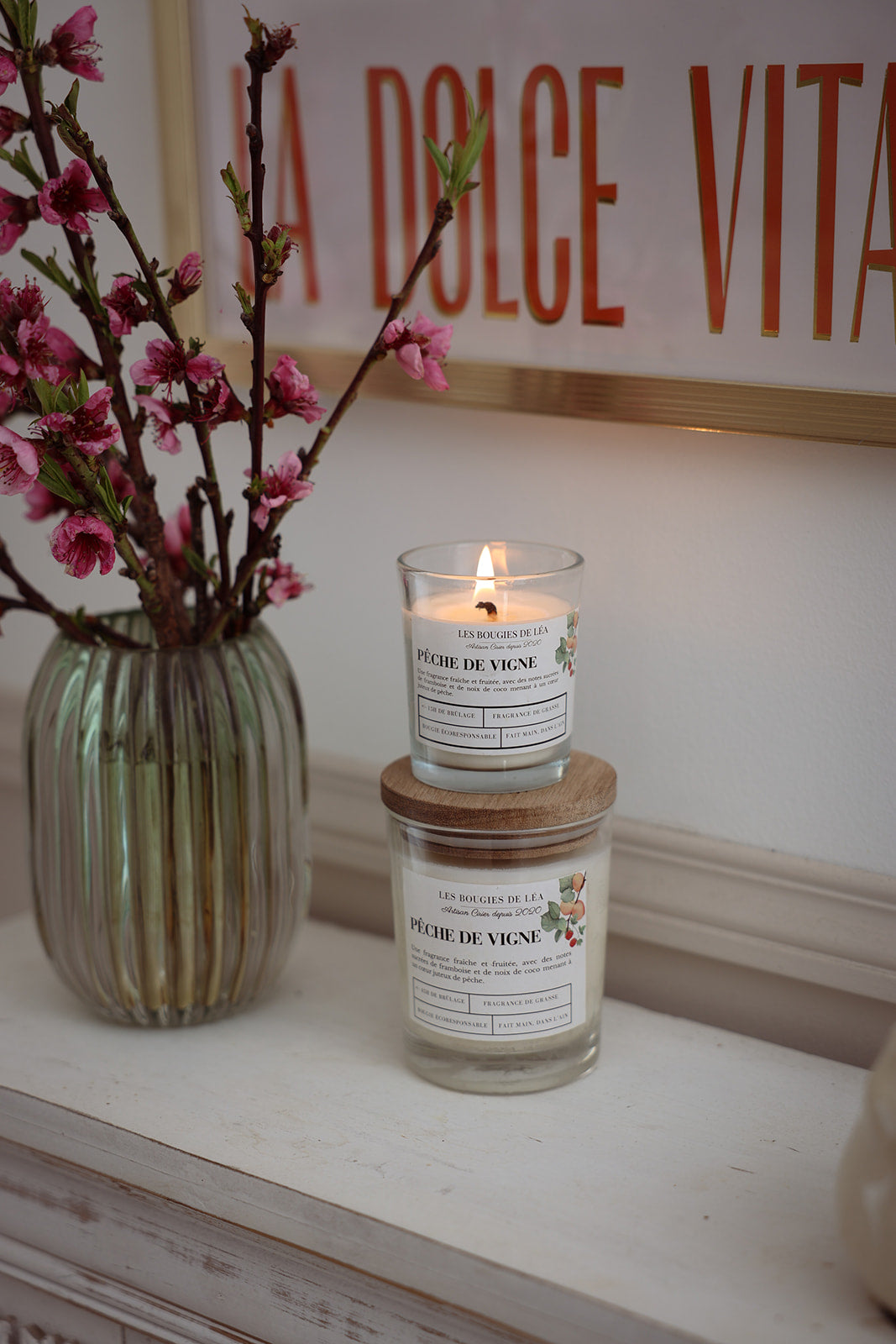 Bougies artisanales parfumées Les Bougies de Léa Pêche de vigne, sur une cheminée bohème chic, accompagnées d'un vase de Fleurs de Cerisier et un table au mur "Dolce Vita" terracotta.