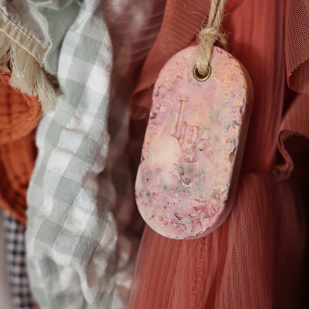 Suspension végétale parfumée artisanale LBL Pêche de vigne rose, dans un dressing, un placard ou penderie devant robe rose.