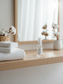 Flacon testeur de 30ml de brume d'ambiance Fleur de Coton LBL posé sur une table en bois à côté de serviettes dans une salle de bain.
